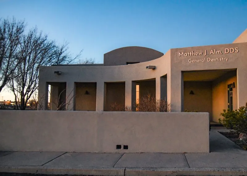 Exterior view of a modern beige stucco building with curved architectural lines and signage reading Matthew J. Alm, DDS General Dentistry.